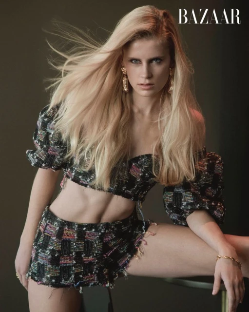 Blonde model poses indoors wearing a two-piece black embellished crop top and skirt, along with gold jewelry and BAZAAR magazine logo.