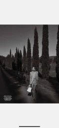 Model Vika Falileeva in a striped suit holding a handbag on a cypress-lined road photographed by Philipp Jelenska.