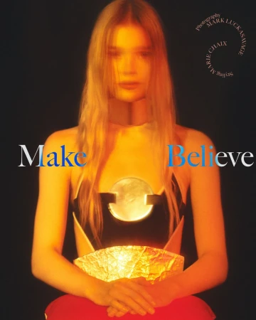 Blonde woman in black and white top with round silver detail, seated in studio with red skirt, holding gold paper art.