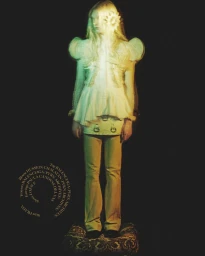 Model standing on a patterned stool against a dark background in a fashion editorial photograph.