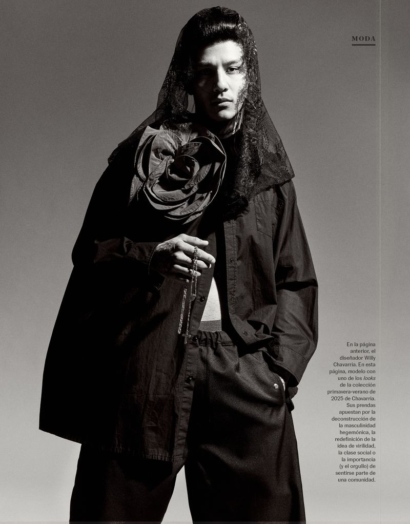 Fashion editorial shot of a slender adult male in dark clothing and a lace veil, holding beads, against a grey gradient background.