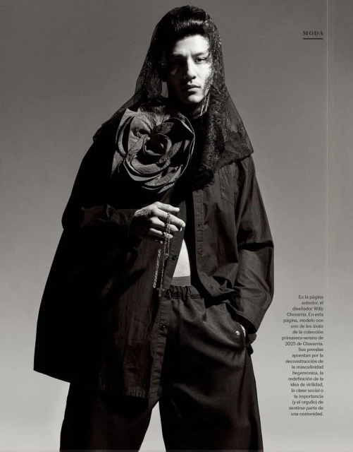 Fashion editorial shot of a slender adult male in dark clothing and a lace veil, holding beads, against a grey gradient background.