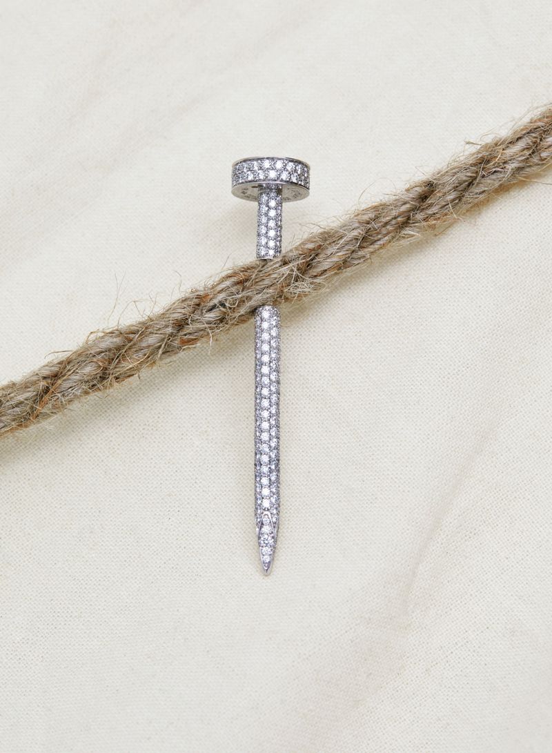 Diamond-encrusted nail jewelry made of white gold, set on a light background with a textured rope detail.