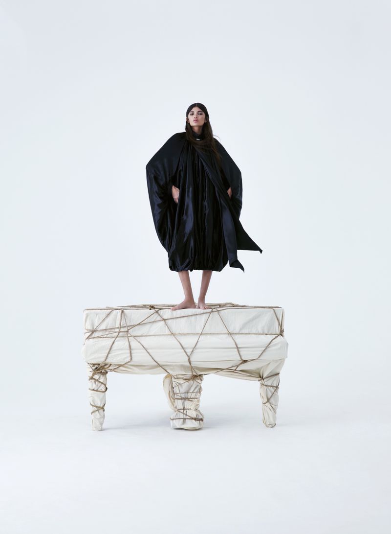 Model standing barefoot on top of a fabric-wrapped, rope-bound piano against a white studio background for Mojeh Magazine