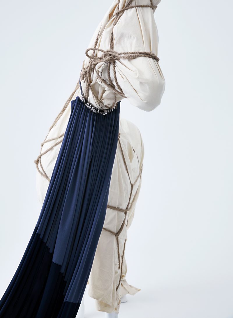 Fabric-covered form with dark flowing fabric, secured with rope, stands in a bright white studio, creating an artful, textured composition.