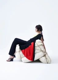Model wearing black clothing seated on a white fabric structure tied with rope against a white background