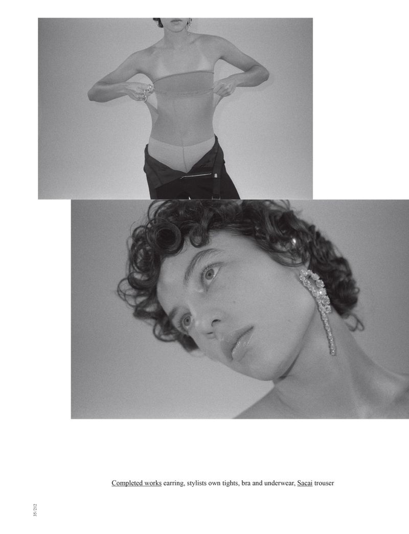 Black and white studio shot of a young adult female model in undergarments and open trousers, with a dramatic earring.