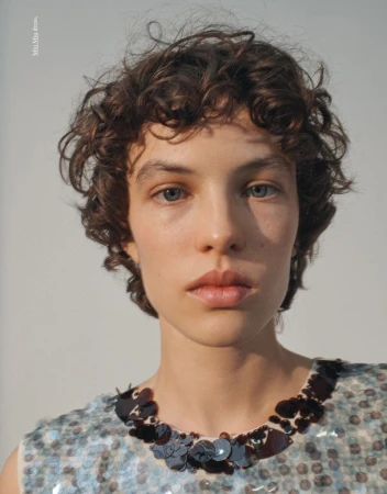 Close-up portrait of a fair-skinned adult female with curly brown hair and blue eyes, wearing a sequined dress with dark trim on white backdrop.
