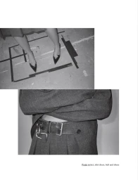 Black and white editorial fashion layout featuring a cropped view of a grey suit jacket, pleated skirt, leather belt with metal hardware, and pointy-toe heels standing on a textured floor.