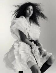 Model Nazarit Machin wearing a white ruffled dress with dark curly hair in motion against a seamless backdrop