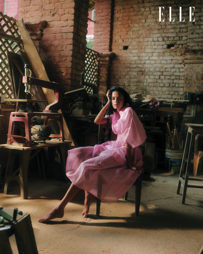 Young woman poses in a pink dress in rustic interior. Brick walls, tables, and studio equipment create an artistic atmosphere.