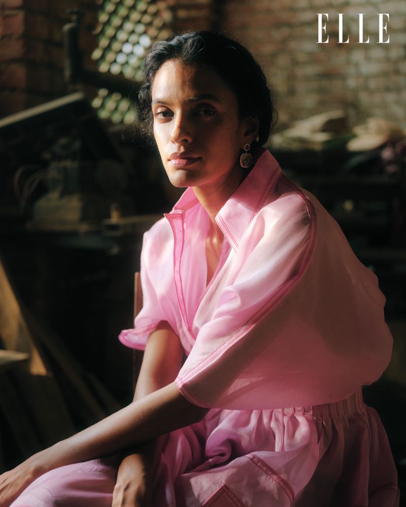 Elegant portrait of an adult woman in a pink dress, seated indoors with soft lighting. The ELLE magazine logo is visible in the upper right.
