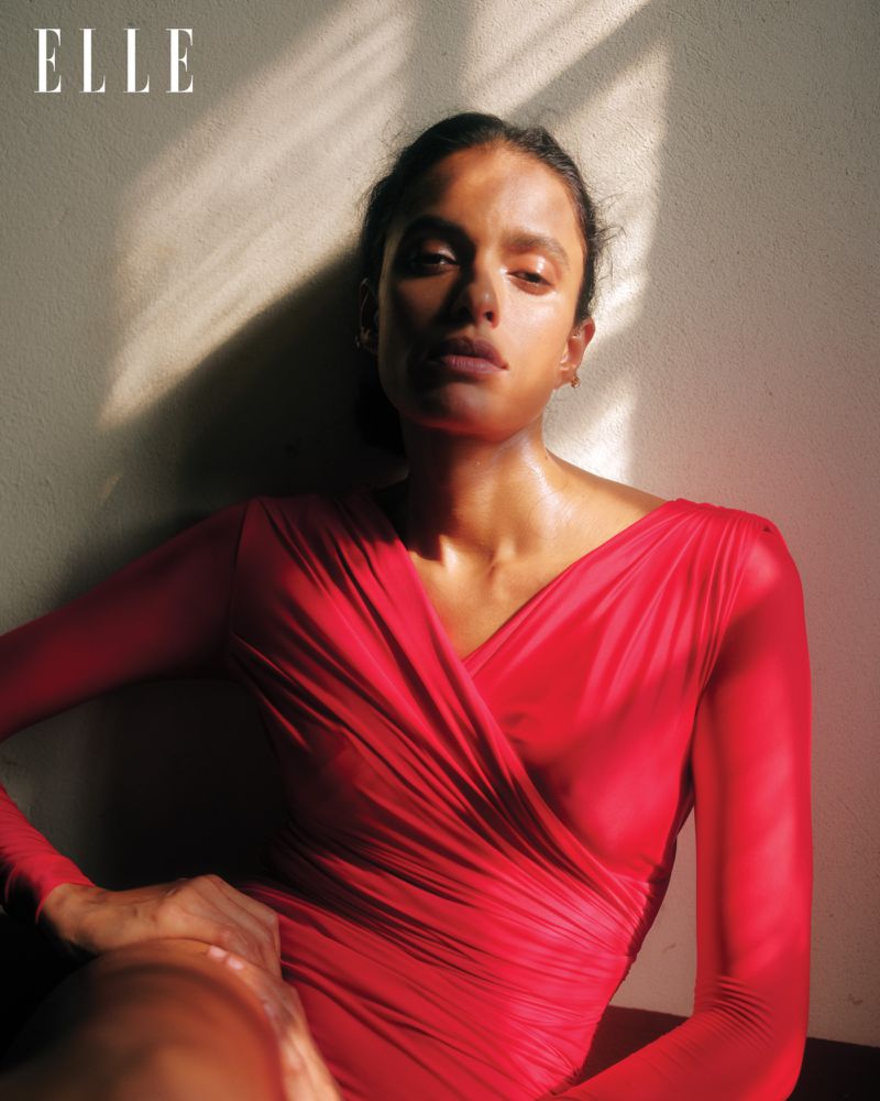 Portrait of a woman in a red dress with long sleeves, sitting in front of a wall with sunlight and shadows. Fashion photography.