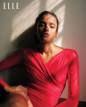 Portrait of a woman in a red dress with long sleeves, sitting in front of a wall with sunlight and shadows. Fashion photography.