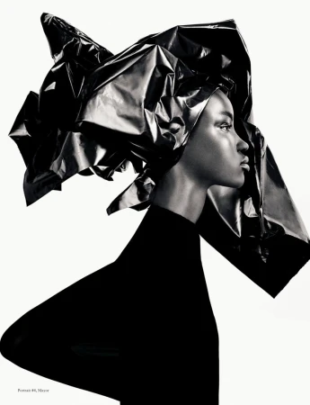 Model in profile wearing a black top and an oversized sculpted black foil headdress against a plain white background.