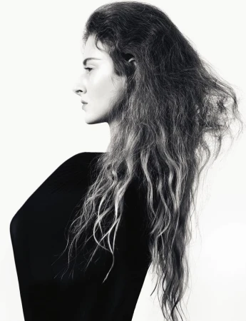 Profile portrait of a woman with long textured hair wearing a black top against a solid white background.