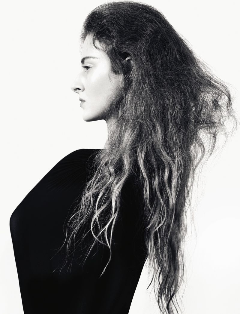 Profile portrait of a woman with long textured hair wearing a black top against a solid white background.