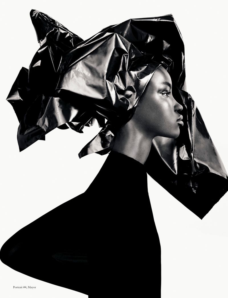Striking black and white fashion portrait of a Black female model wearing a large, sculpted headpiece against a clean white background.