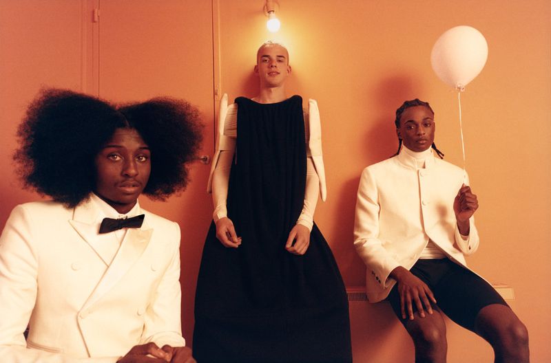 Three stylishly dressed people in a studio setting. One holds a white balloon, adding a playful touch to the portrait.