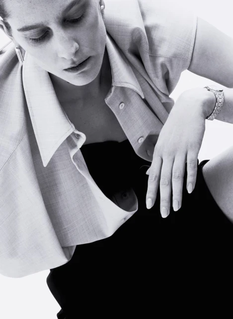 Monochrome studio portrait of a stylish adult woman wearing a shirt, strapless top, and a bracelet, looking down in soft lighting.