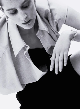 Monochrome studio portrait of a stylish adult woman wearing a shirt, strapless top, and a bracelet, looking down in soft lighting.
