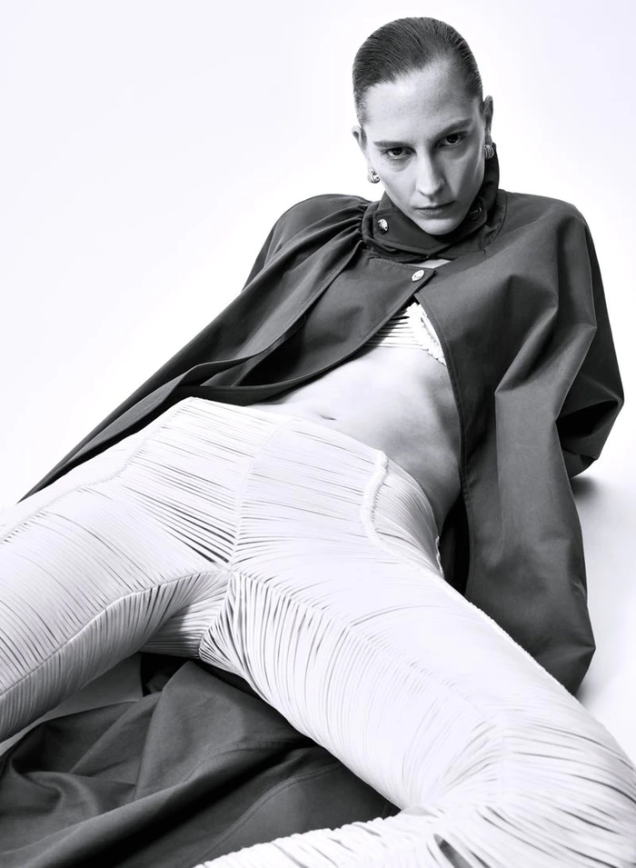 Model Ros Georgiou wearing textured white pants and a dark coat against a white background for L'Officiel Italia editorial