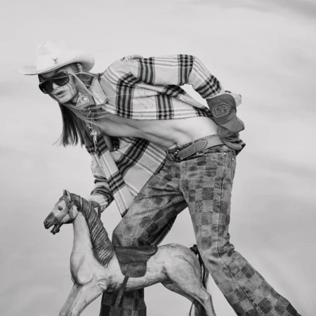 Fashion shot in black and white of person wearing cowboy hat, sunglasses, and flannel shirt while riding toy horse.