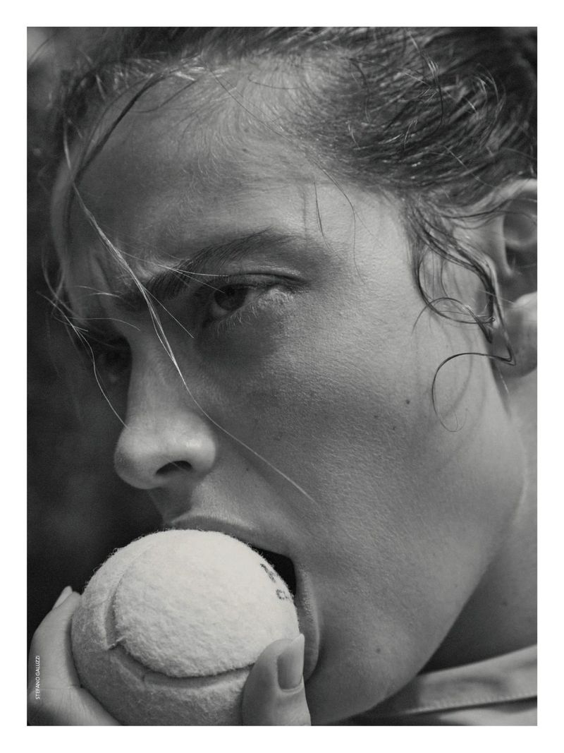 Black and white portrait of an adult female biting a tennis ball, close-up shot focused on face and ball.