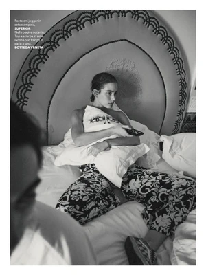 Model seated on a bed holding a pillow with a graphic eye design, photographed in black and white for Marie Claire Italia.