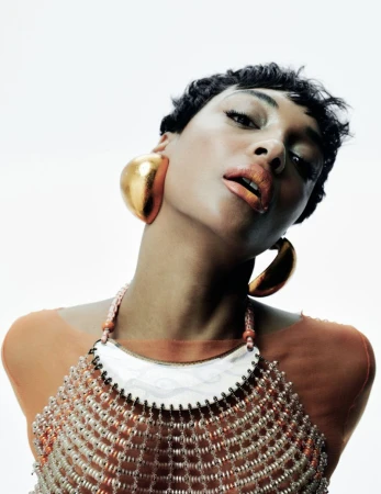Headshot of an adult woman with short dark hair, large gold earrings, and beaded jewelry against a bright white background. Beauty portrait.
