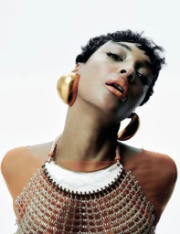 Jourdan Dunn wearing statement gold earrings and beaded necklace against a white background for Harper's Bazaar España