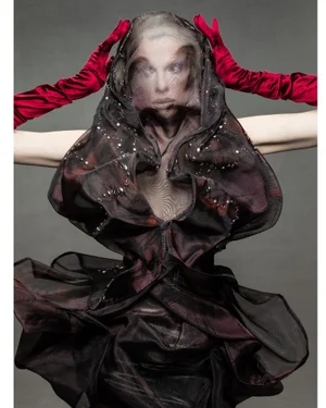 Julia Fox wearing a dark sheer hooded dress and red gloves with her face covered by a veil for Tush Magazine.