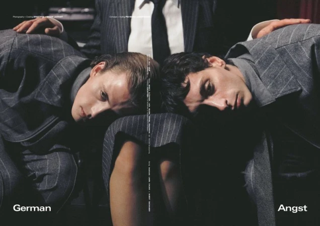 Two adult males in pinstripe suits rest their heads together. The composition creates a symmetrical, mirrored effect, and the photograph has a subdued aesthetic.