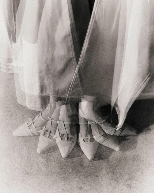 Low angle, monochrome shot of a person in a white dress with multiple exposures of white pointed shoes on a light grey surface.