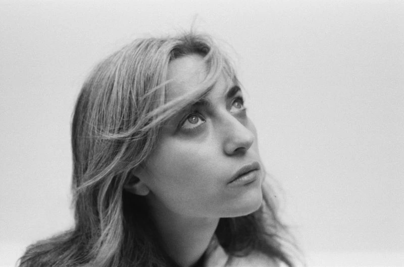 Close-up black and white portrait of a blonde woman looking up with a thoughtful expression against a bright, neutral background.