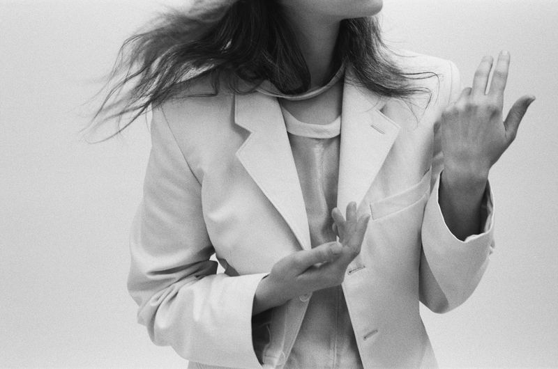 Monochrome shot of a woman in an open blazer with hands posed against a plain backdrop, evoking modern fashion and minimalist style.