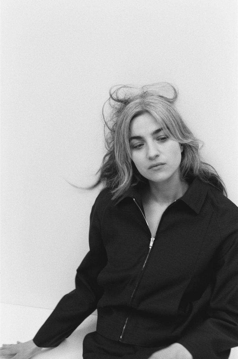 Portrait of a woman wearing a black zip jacket against a plain white background for Interlope Magazine.