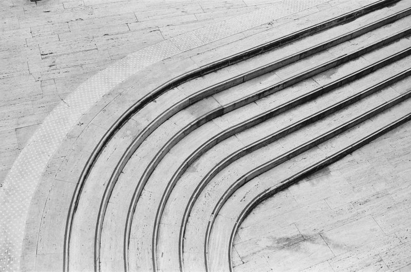 Abstract high-angle shot of curving outdoor concrete stairs creating a textured, minimalist architectural composition in black and white.