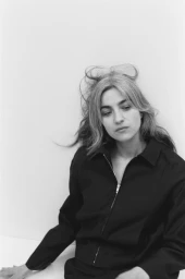 Portrait of a woman wearing a black zip jacket against a plain white background for Interlope Magazine.