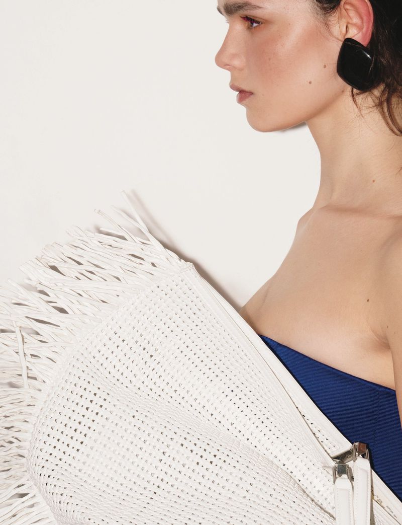 Profile of a fair-skinned woman with dark earrings, a blue top, and a white textured textile against a plain white background.