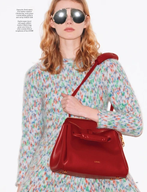 Woman with red handbag in fashion shot wearing aviator sunglasses and patterned dress against white backdrop.