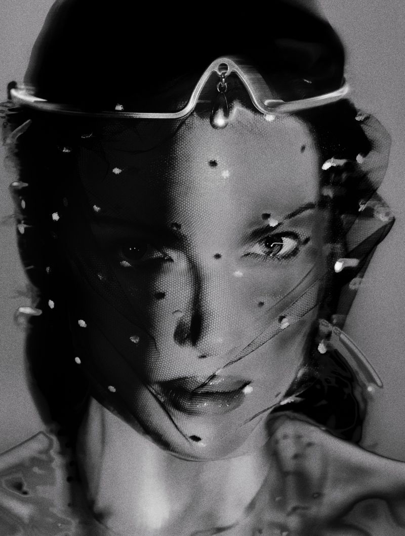 Dramatic black and white portrait of a woman with a sheer, spotted veil and decorative headpiece, close-up shot with shallow depth of field.