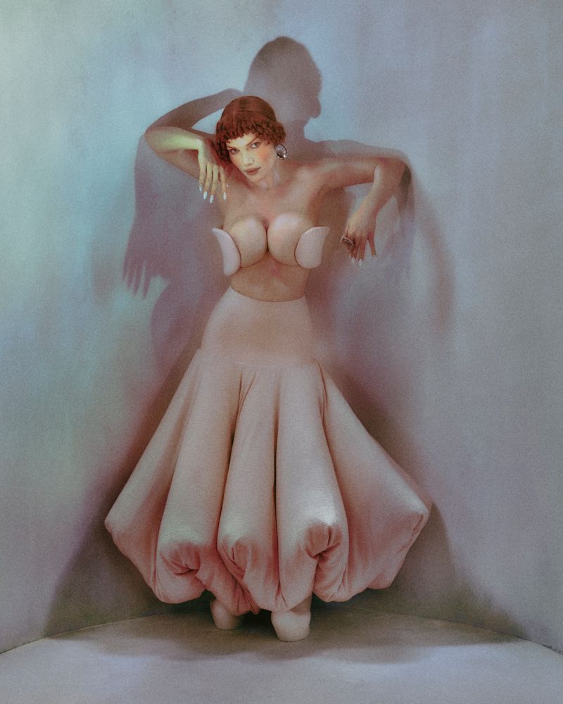 Elegant woman in a light pink dress posing in a corner with a shadow on the wall, artistic fashion photography.