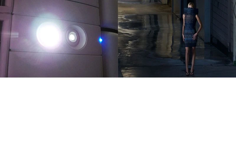 Woman in futuristic dress poses in an underground tunnel as a bright light shines on an architectural wall in the background.