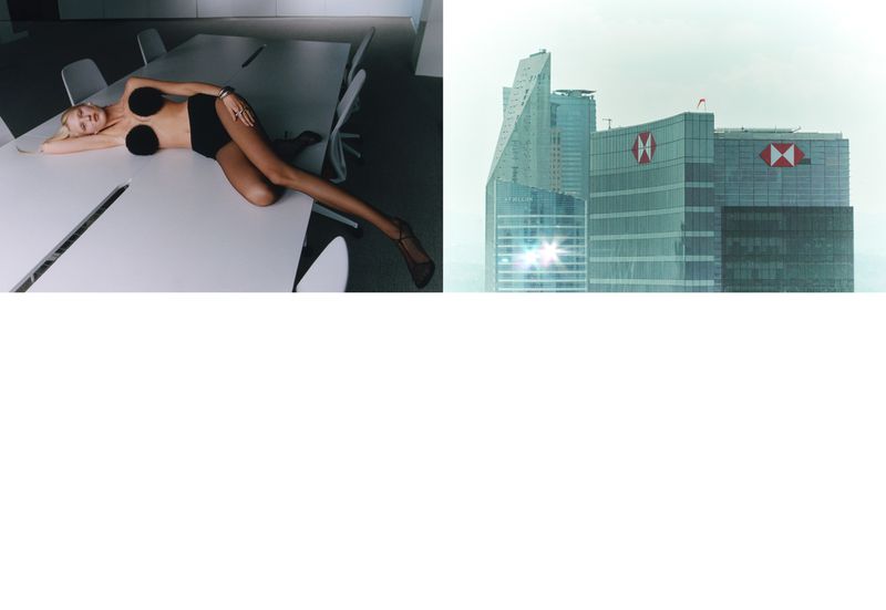 Fashion shot of a woman lying on a white table in a black swimsuit with city buildings in the background against a light sky.