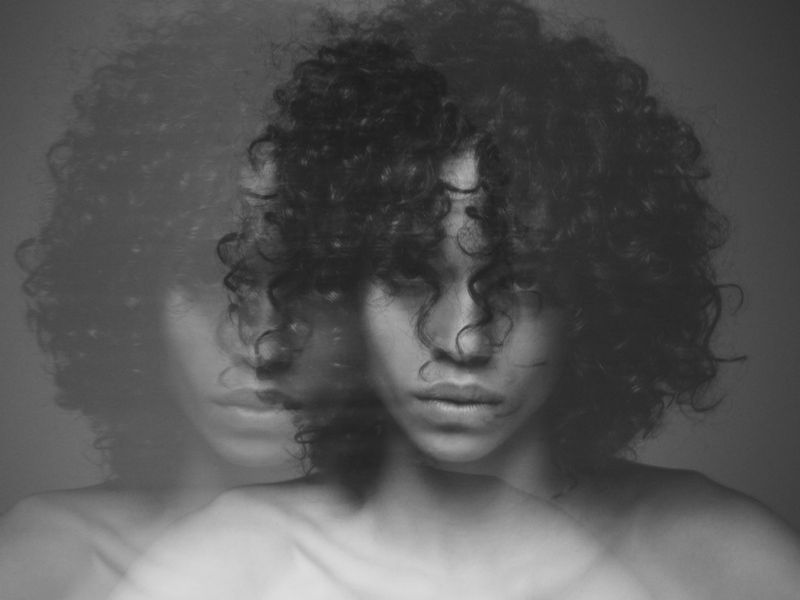 Monochrome multiple exposure portrait of a model with dark curly hair and intense expression.