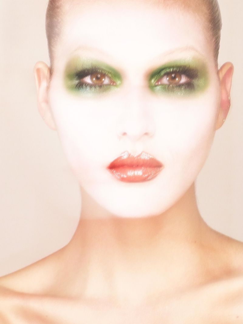 Close-up portrait of a woman with green eyeshadow and glossy red lipstick, soft focus, beauty shot, fair skin, looking at the camera.