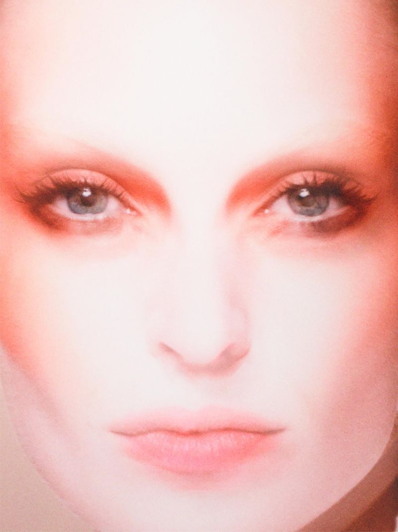 Close-up portrait of a woman's face with makeup, featuring soft lighting and a focus on her blue eyes and fair complexion.