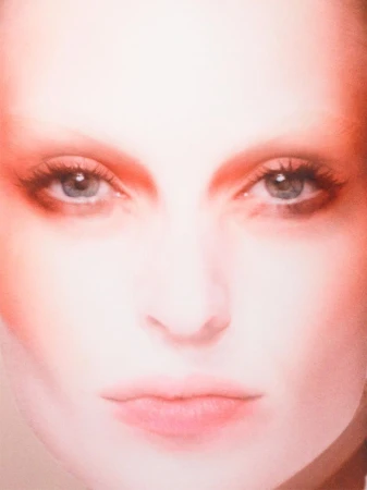 Close-up portrait of a woman's face with makeup, featuring soft lighting and a focus on her blue eyes and fair complexion.