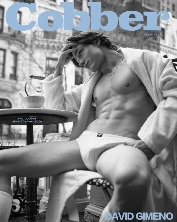 Black and white magazine cover featuring a shirtless man in underwear and robe sitting outside on a balcony with a city view.